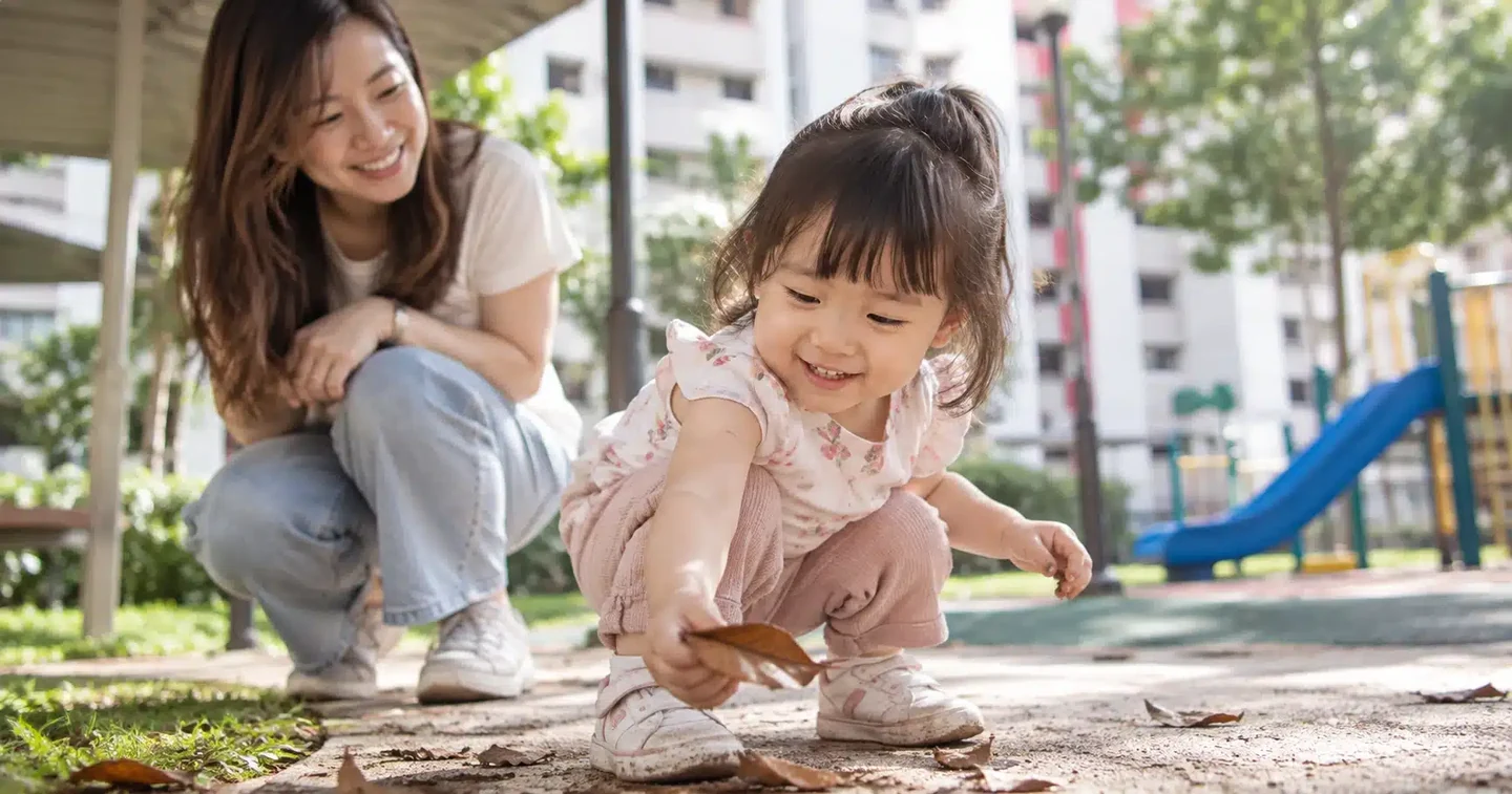 A mother and young child playing with leaves at a playground